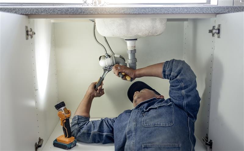 Plumber repairing pipes beneath a bathroom sink in North Miami Beach