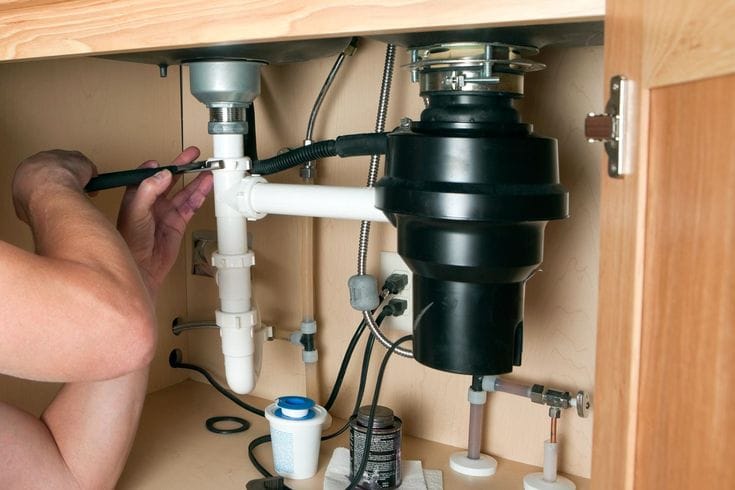 Plumber installing a garbage disposal beneath a kitchen sink in North Miami Beach