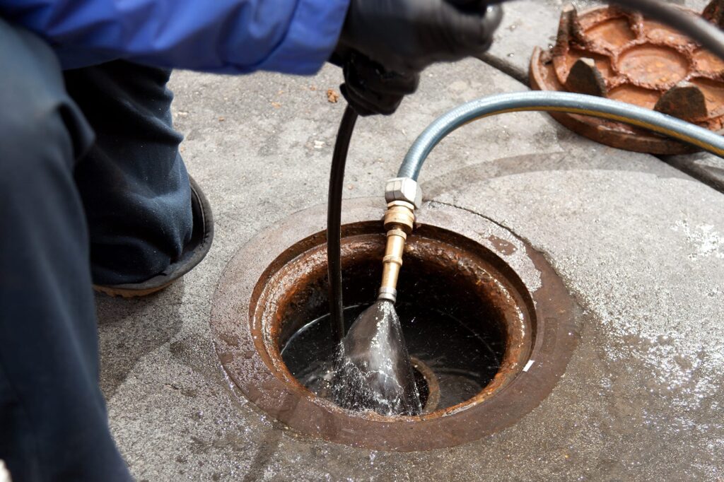 Plumber hydro jetting a sewer line through a manhole in North Miami Beach