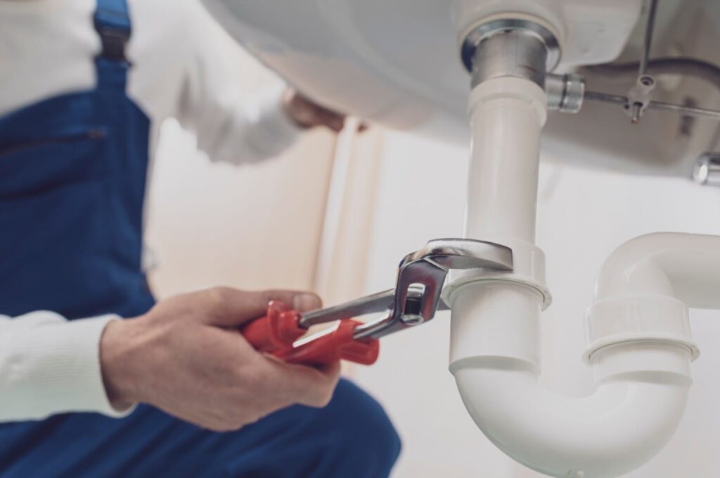 Plumber repairing a white drain pipe beneath a sink in North Miami Beach