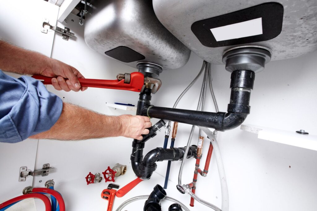 Plumber repairing drain pipes beneath a kitchen sink in North Miami Beach
